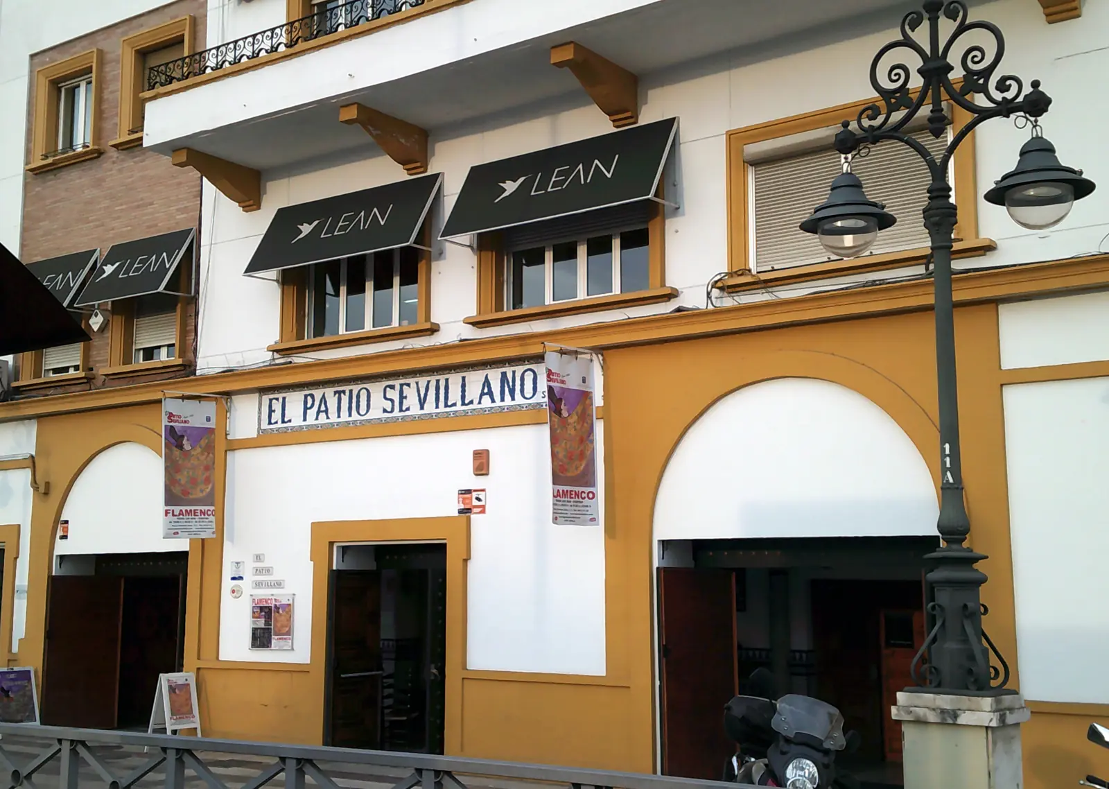 The facade of the building on Paseo de Cristóbal Colón, with a blue tile sign reading El Patio Sevillano above two arched doorways